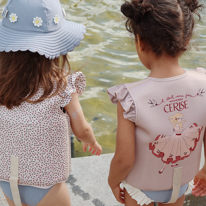 Mädchen stehen am Wasser und tragen Schwimmwesten mit Blumenmuster und mit einem Prinzessinnenprint von Konges Slojd.