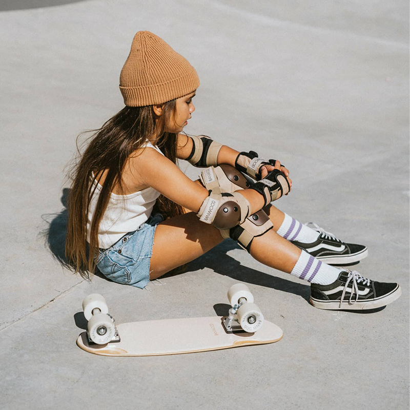 Mädchen mit Banwood Skateboard und Schutzausrüstung für Knie, Ellbogen und Handgelenke in der Farbe Creme