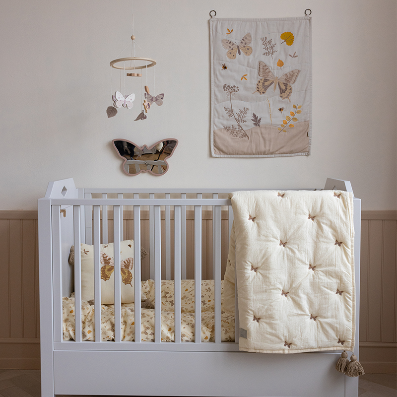 Wandteppich für Kinder in Beige mit Blumen und Schmetterlingsmotive von Cam Cam Copenhagen hängt über Babybett.