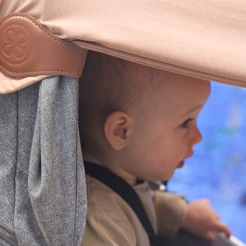 Kind sitzt im Kinderwagen am Verdeck ist eine braune UV-Decke von Cloby befestigt. 