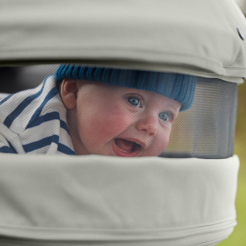 Joolz Geo 3 in Sage Green mit Babywanne und baby das aus Belüftungsfenster raus schaut