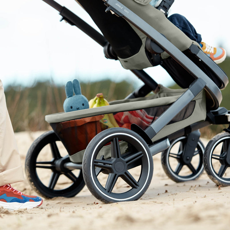 Joolz Geo 3 in Sage Green mit Sitzeinheit und Strandspielzeug im Korb am Strand 