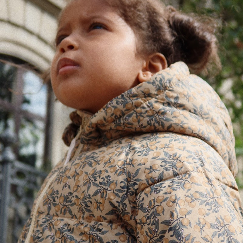 Kind trägt die lange Puffer-Jacke / Daunen-Jacke von Konges Sløjd mit süssem Print &quot;Orangerie Beige&quot;