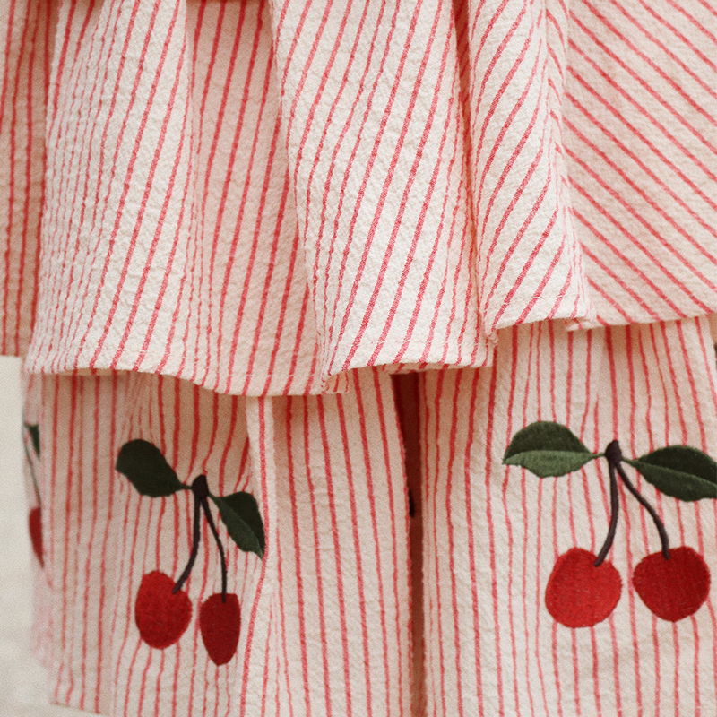 Kinder Sommerkleid mit Träger in Beige mit roten Streifen und Kirschstickereien am Saum von Konges Slojd. Nahaufnahme von den Kirschstickereien.
