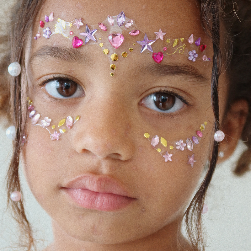 Mädchen trägt um die Augen die Strasssteinchen fürs Gesicht für Kinder mit Steinchen in Lila, Rosa und Pink von Konges Slojd.