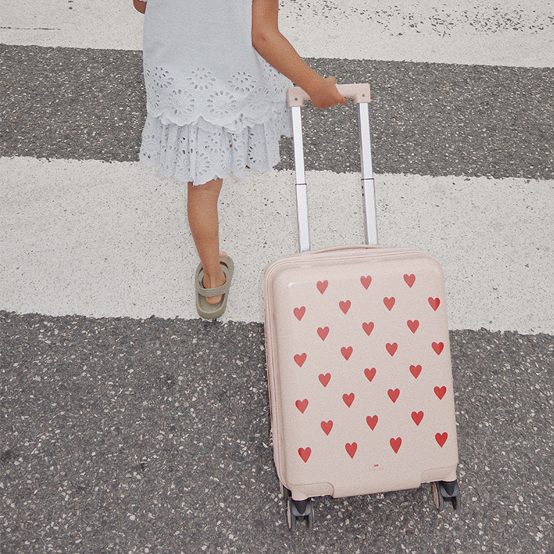 Mädchenhand zieht Reisekoffer in Rosa für Kinder mit Herzchenmuster von Konges Slojd.