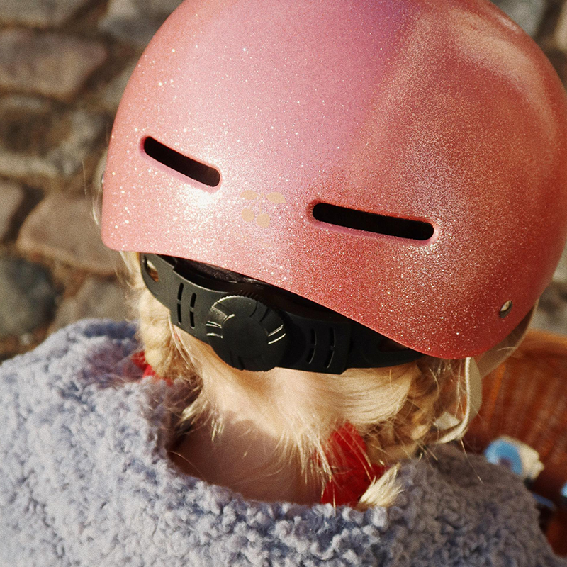 Nahaufnahme von Mädchen von hinten, das einen pinken, glitzernden Kinderhelm von Konges Slojd trägt. 