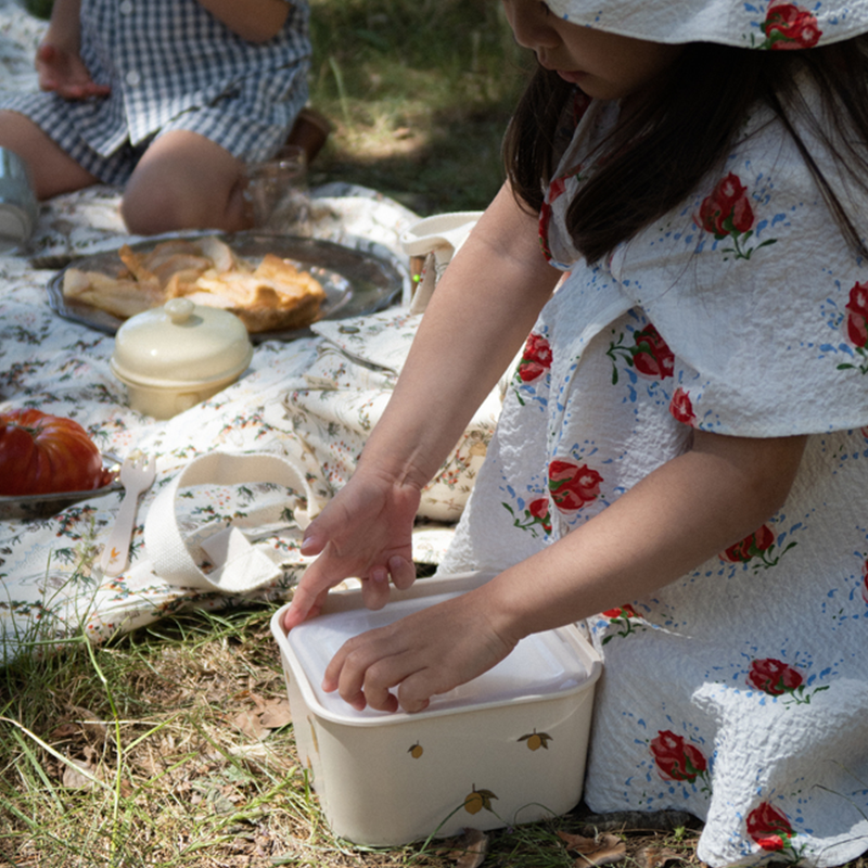 Mädchen beim Picknick mit einer Lunchbox in Beige mit Zitronemuster von Longes Slojd.