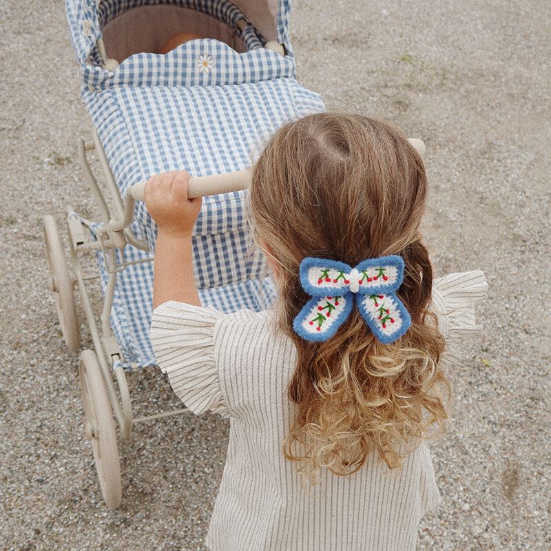 Mädchen schiebt den Blau-weiss karierter Kinderwagen im Vintage Stil für Puppen von Konges Slojd.