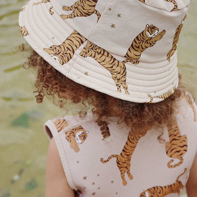 Aufnahme von hinten von einem Kind das Schwimmweste und einen Hut für Kinder in Beige mit Tiger-und Sternenprint von Konges Slojd.