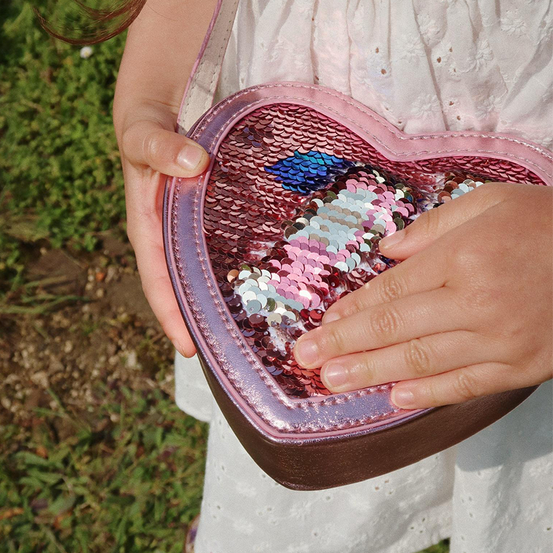 Kinderhände spielen mit den Pailletten von der Umhängetasche in Herzform mit Pailletten in Rosa von Konges Slojd. 