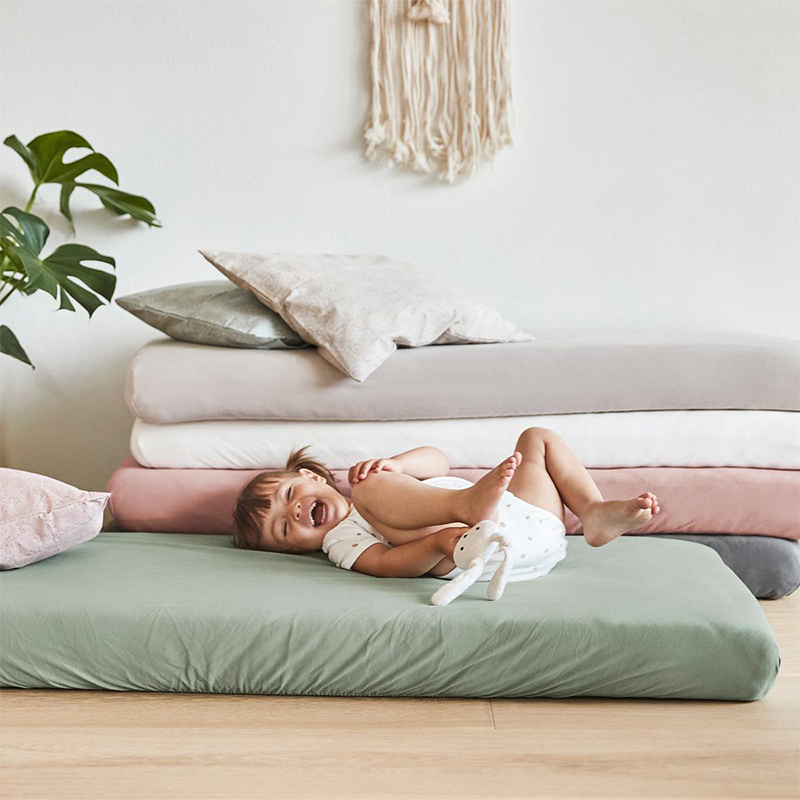 Aufgetürmte Kindermatratzen mit verschiedenfarbigen Fixleintücher. Mädchen spielt auf einer Matratze.