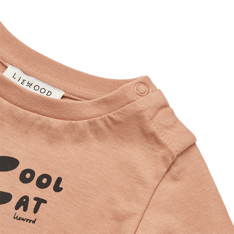 Nahaufnahme vom Schulterknopf vom T-Shirt für Babys in Rosa mit Katzenprint auf dem Bauch von Liewood.
