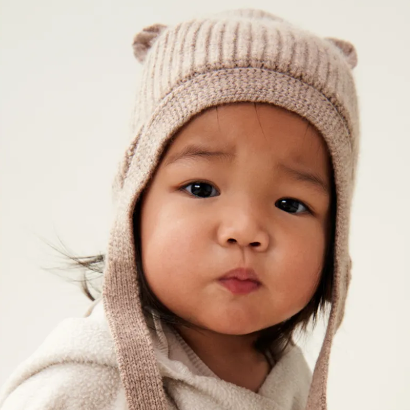 Kleinkind trägt Wollstrickmütze für Kinder in Beige mit Bärchenöhrchen und Bändel von Liewood.