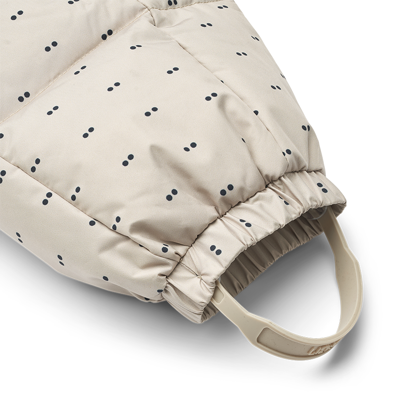 Daunen Schneeanzug in Beige für Babys mit zarten blauen Punkten von Liewood.  Nahaufnahme von der Fussschlaufe. 