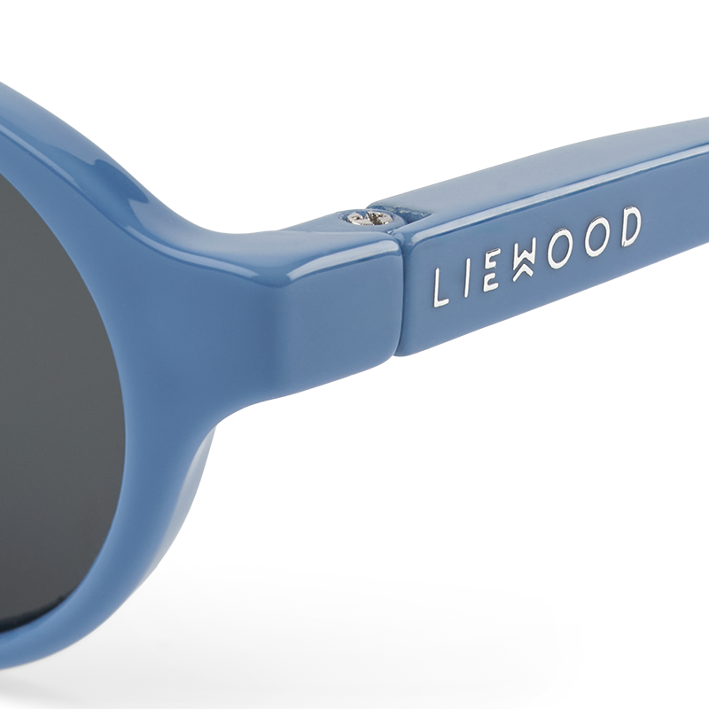 Nahaufnahme von der silbrigen Liewood Aufschrift auf dem Brillenrahmen der Babysonnenbrille mit blauem Rahmen und blauem Silikonband von Liewood. 