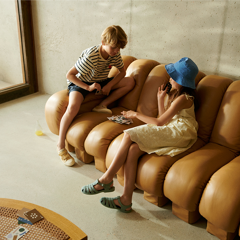 Kinder spielen auf einem Sofa und tragen Liewood Kindersandalen. 