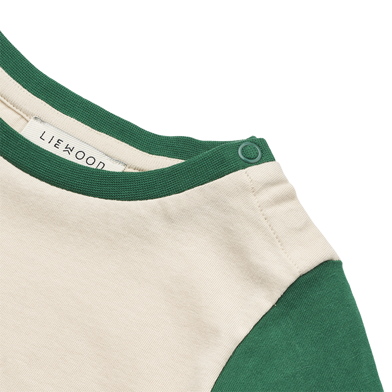 Nahaufnahme vom Druckknopf an der Schulter vom Langarm Shirt für Babys in Beige mit grünen Ärmeln und grünem Print von Liewood.