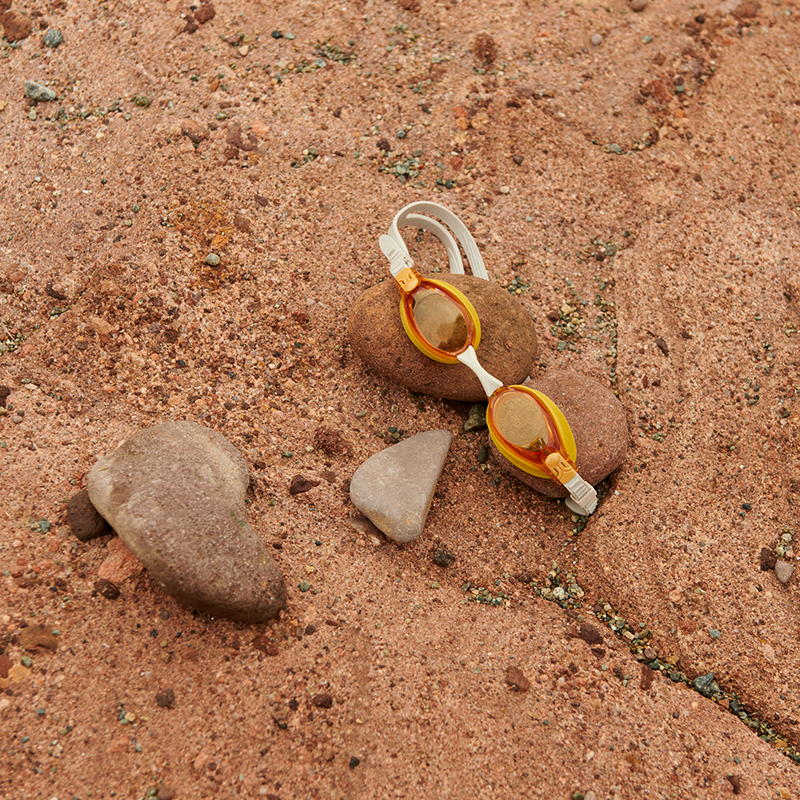  Liewood Schwimmbrille &#39;Titas&#39;  in Orange auf Steinen.