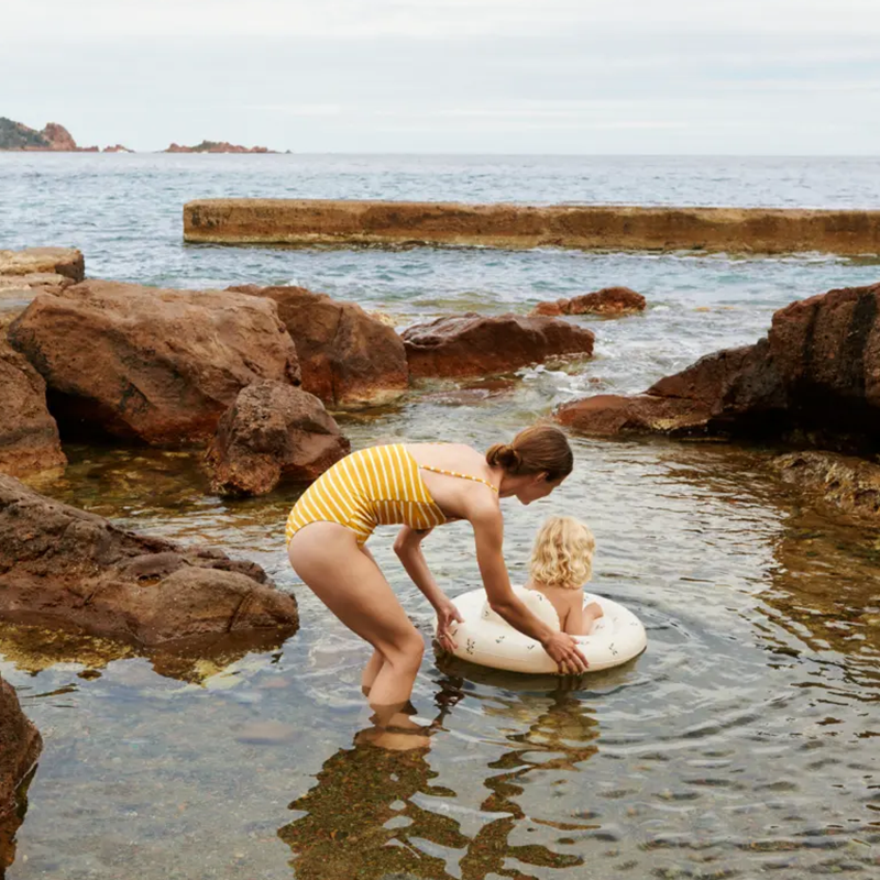 Frau spielt mit Baby im Wasser. Baby sitzt in einem Schwimmreifen für Babys mit Sitz in Beige und mit Pfirsichmuster von Liewood. 