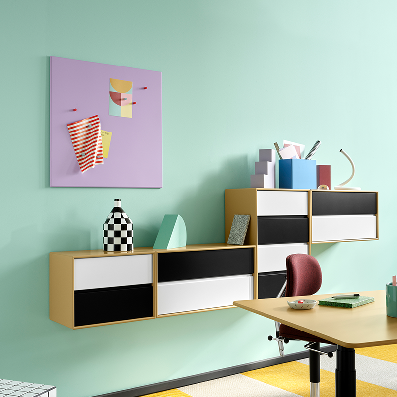 Magnettafel in lila mit passenden Magneten von Montana hängt über Schreibtisch an einer mintfarbenen Wand hängt über einem Regal.