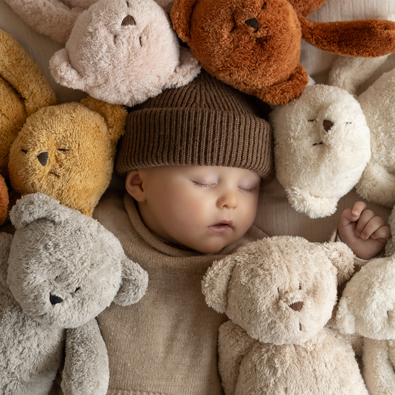 Baby liegt zwischen kuscheligen Teddybören in Grau, Weiss, Beige und Braun von Moonie.
