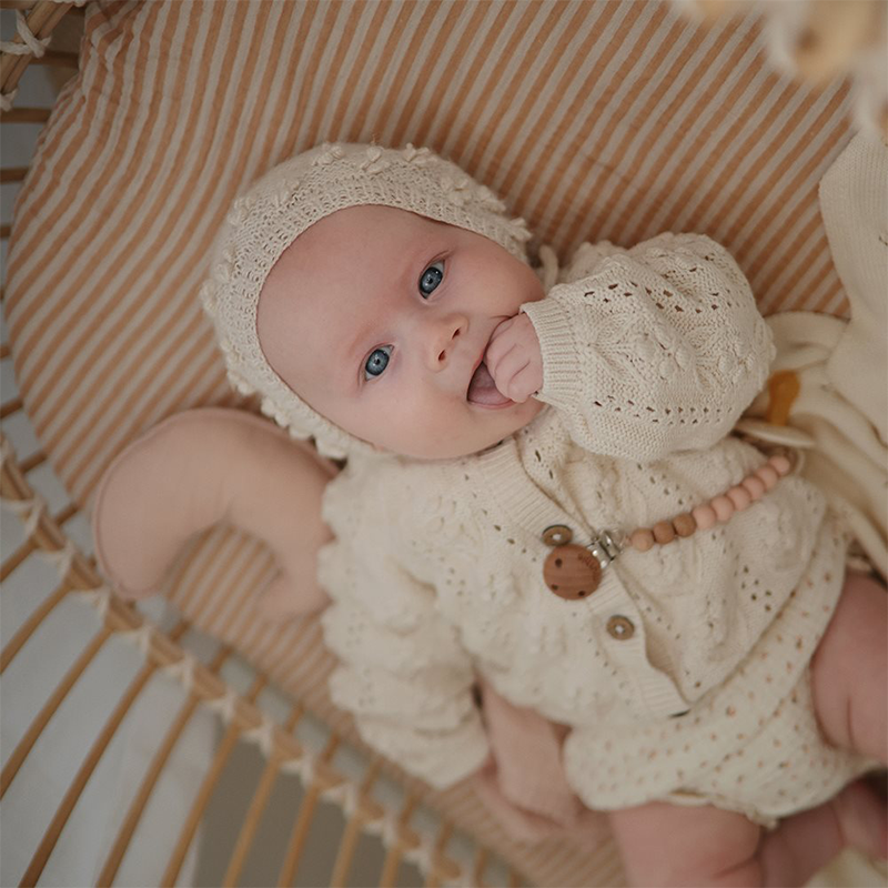 Mushi Schnullerclip Eva in der Farbe Blush, der an der Kleidung des Babys befestigt ist. 