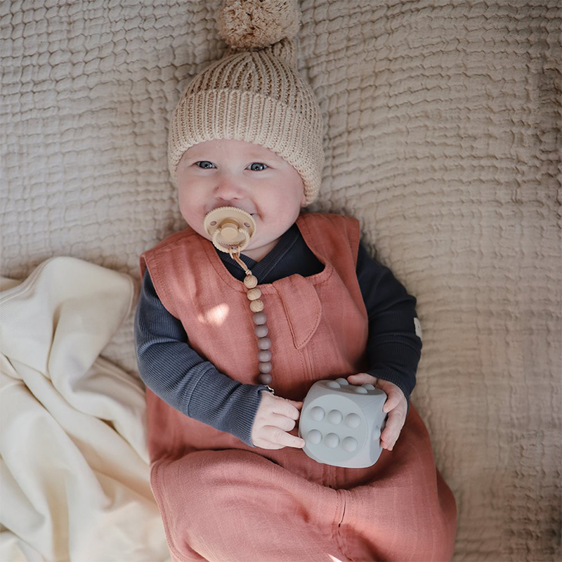 Baby trägt den Schnuller an der Mushie Schnullerkette in Grau. 