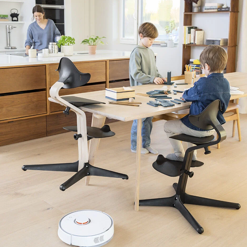 Junge sitzt am Tisch auf Nomi Hochstuhl für Kinder in Schwarz von Stokke. Ein anderer Hochstuhl ist auf dem Tisch aufgestuhlt und der zweite Junge spielt im Stehend am Tisch. 