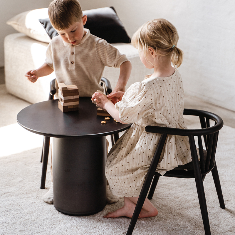 2 Kinder sitzen auf schwarz gebeizten Kinderstühlen von Oaklings an einem Kindertisch und spielen mit Spielsteinen.