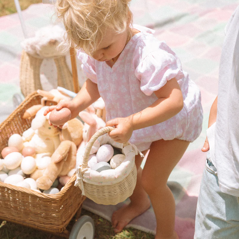 Kind füllt einen kleinen Rattankorb von Olli und Ella mit bunten Ostereiern.