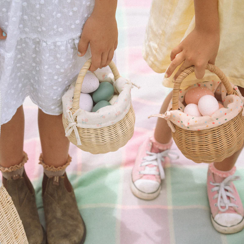 2 Kinderhände tragen je einen kleinen Rattenkorb von Ollie und Ella gefüllt mit bunten Ostereier.