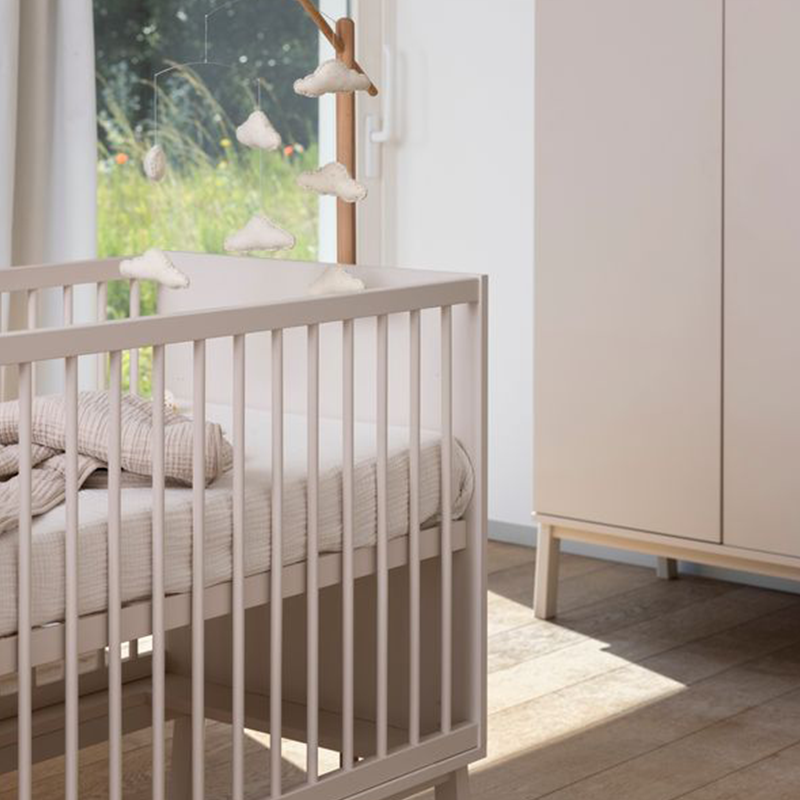 Babybett steht in einem lehmfarbigen Grauton steht in einem Babyzimmer.