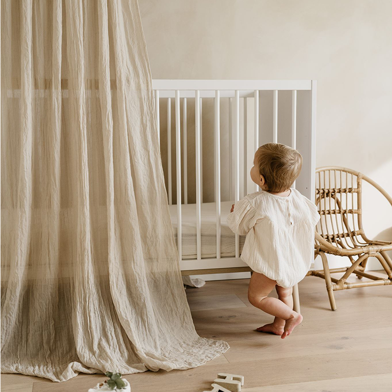 Baby steht an seinem Babybett in Weiss mit Beinen aus Eiche von Quax mit Baldachin.