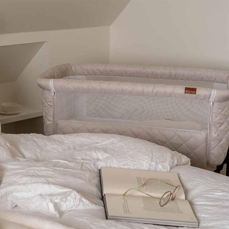 Beistellbett für Babys  in Beige mit schwarzem Gestell von Quax steht neben dem Elternbett.