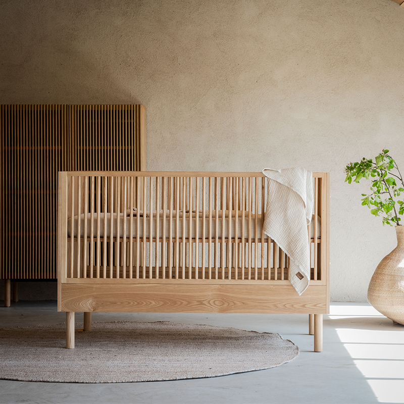 Babybett in Eschenkoptik in Kinderzimmer mit Schrank im Hintergrund von Quax.