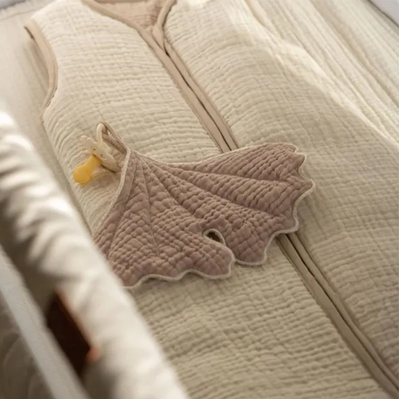 Kinderschlafsack in Beige von Quax liegt im Babybett.