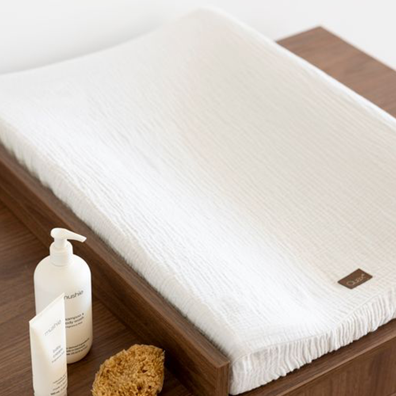Aufnahme von oben von Wickelkommode in Kastanienbraun mit drei Schubladen von Quax mit Wickelkissen in Weiss und mit Pflegeprodukten fürs Baby drauf.