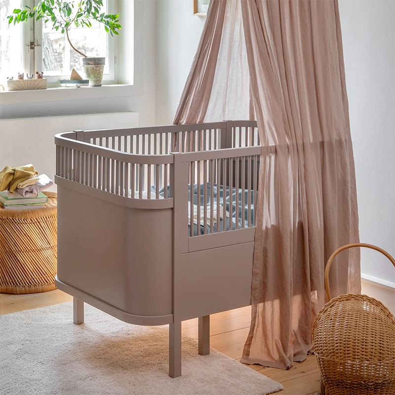 Sebra Baby- und Juniorbett in Beige. steht in einem Babyzimmer und besitzt einen Betthimmel.