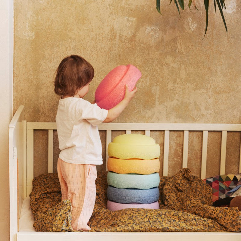 Kind spielt auf Kinderbett mit Set mit 6 Stapelsteinen in schönen Regenbogenfarben in Pastell