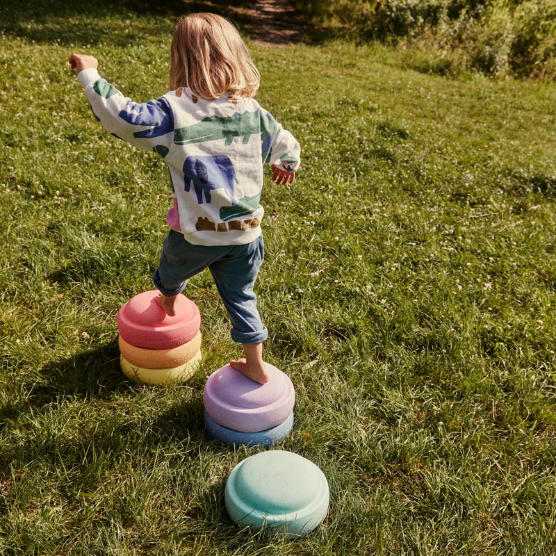 Kind spielt im Garten mit den Stapelsteinen in Pastell