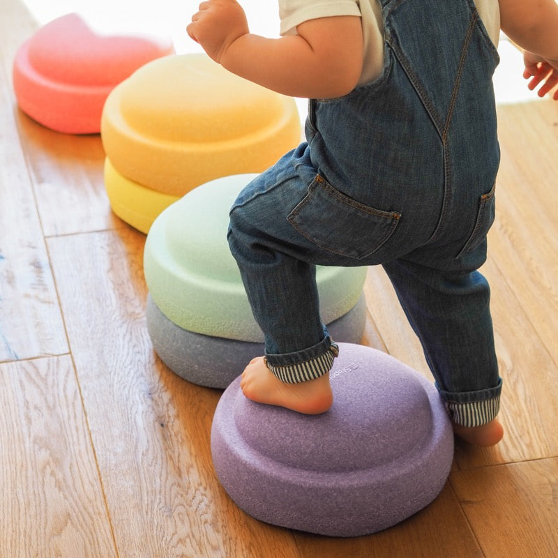 Kleinkind balanciert über die Pastellfarbenen Stapelsteine in Regenbogenfarben