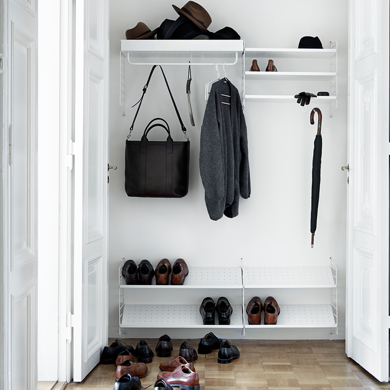Garderobe mit String Schuhregalen in weiss und Wandregal mit Haken und Stange an der Taschen und Jacken aufgehängt sind. 