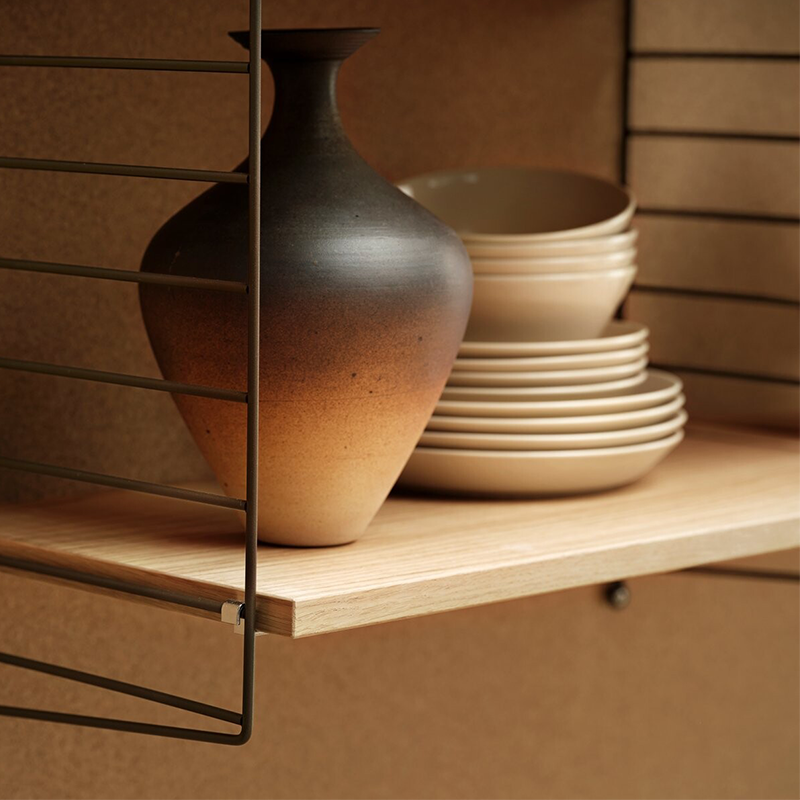 Nahaufnahme von String Regalsystem mit Regalboden in Eiche auf der Eine Vase, Teller und Schüssel stehen. 