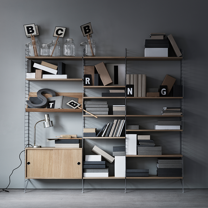 String Furniture Regalsystem mit Regalböden in Eiche Gitterleitern in Grau und einem Schrankelement mit Schubladen in Eiche. 