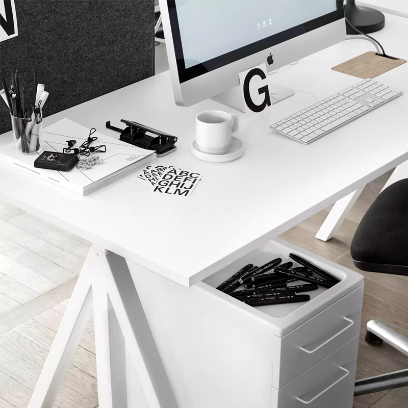 Höhenverstellbarer Schreibtisch in Weiss mit Bildschirm, Tasse und Büroutensilien drauf. Unter dem Tisch steht ein Schubladensystem in Weiss. 