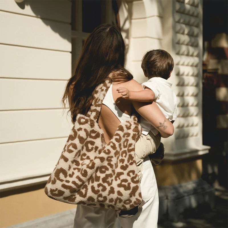 Mama trägt Baby auf dem Arm und hat die Grosse Tragetasche aus flauschigem Teddystoff mit Leopardenmuster von Studio Noos über der Schulter.