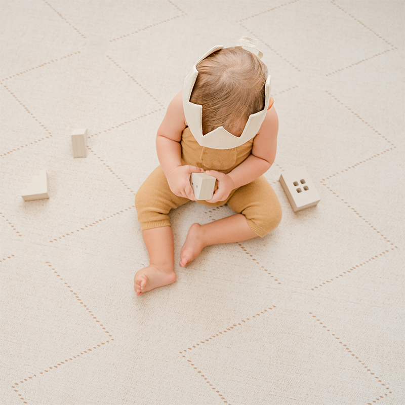 Kleinkind spielt auf der Bodenmatte Tulum von Toddlekind in der Farbe Bone.