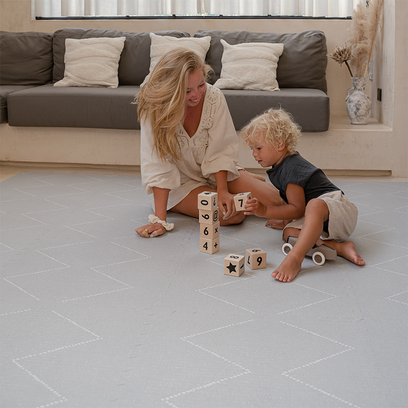 Mama und Junge spielen mit Bauklötzen auf der Toddlekind Spielmatte Tulum in der Farbe Stone.