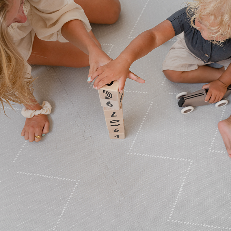 Mama und Kind bauen Turm auf der Toddlekind Spielmatte Tulum in der Farbe Stone.